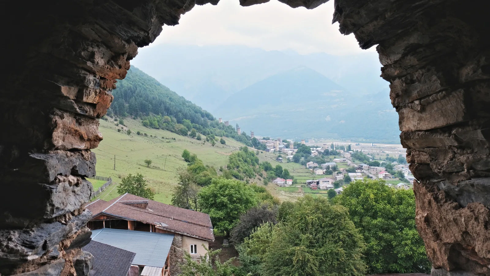 A summer view through the arched window of a Svan tower.