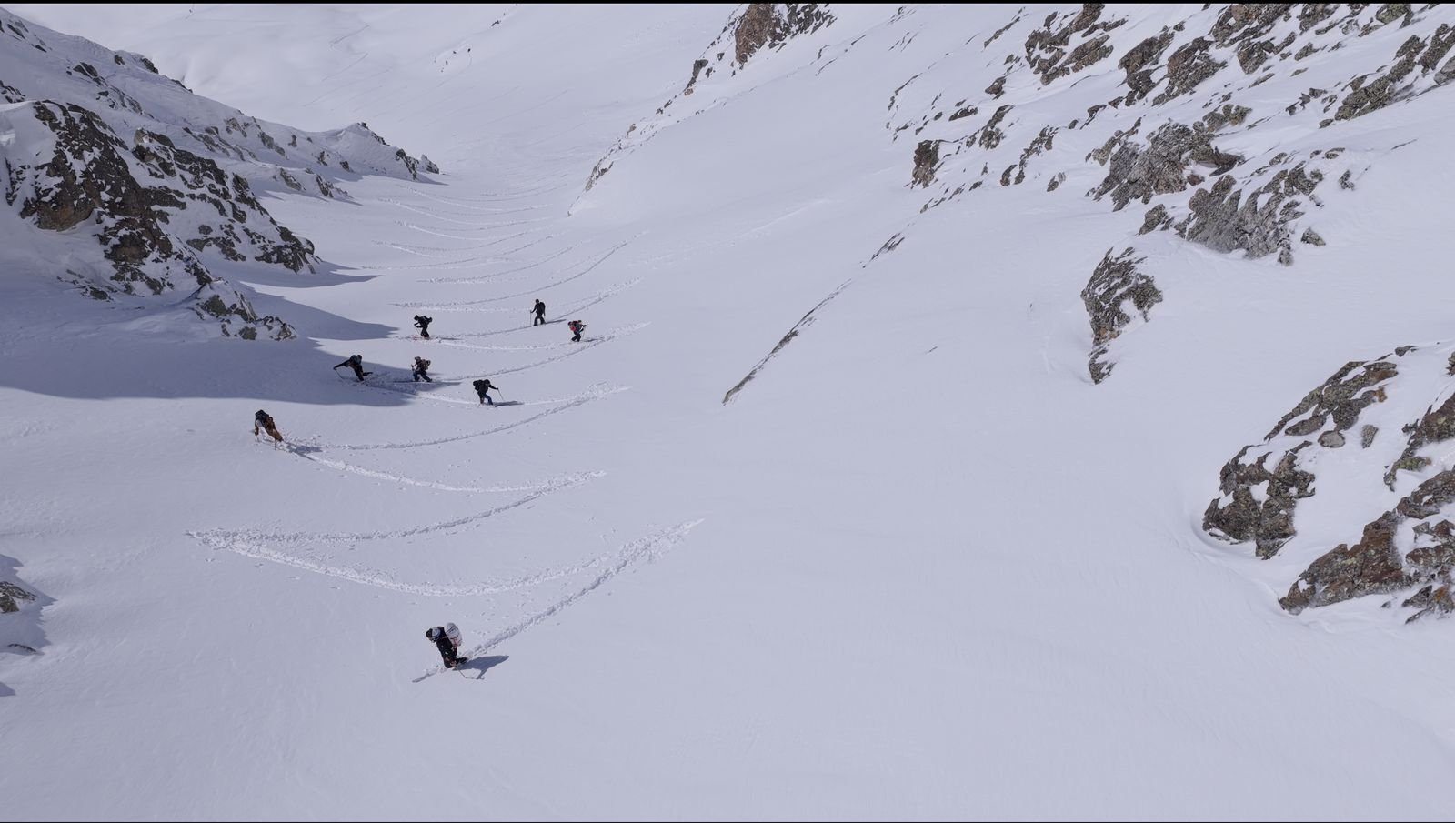 Ski touring group crossing a high alpine bowl, leaving a line of tracks in fresh snow
