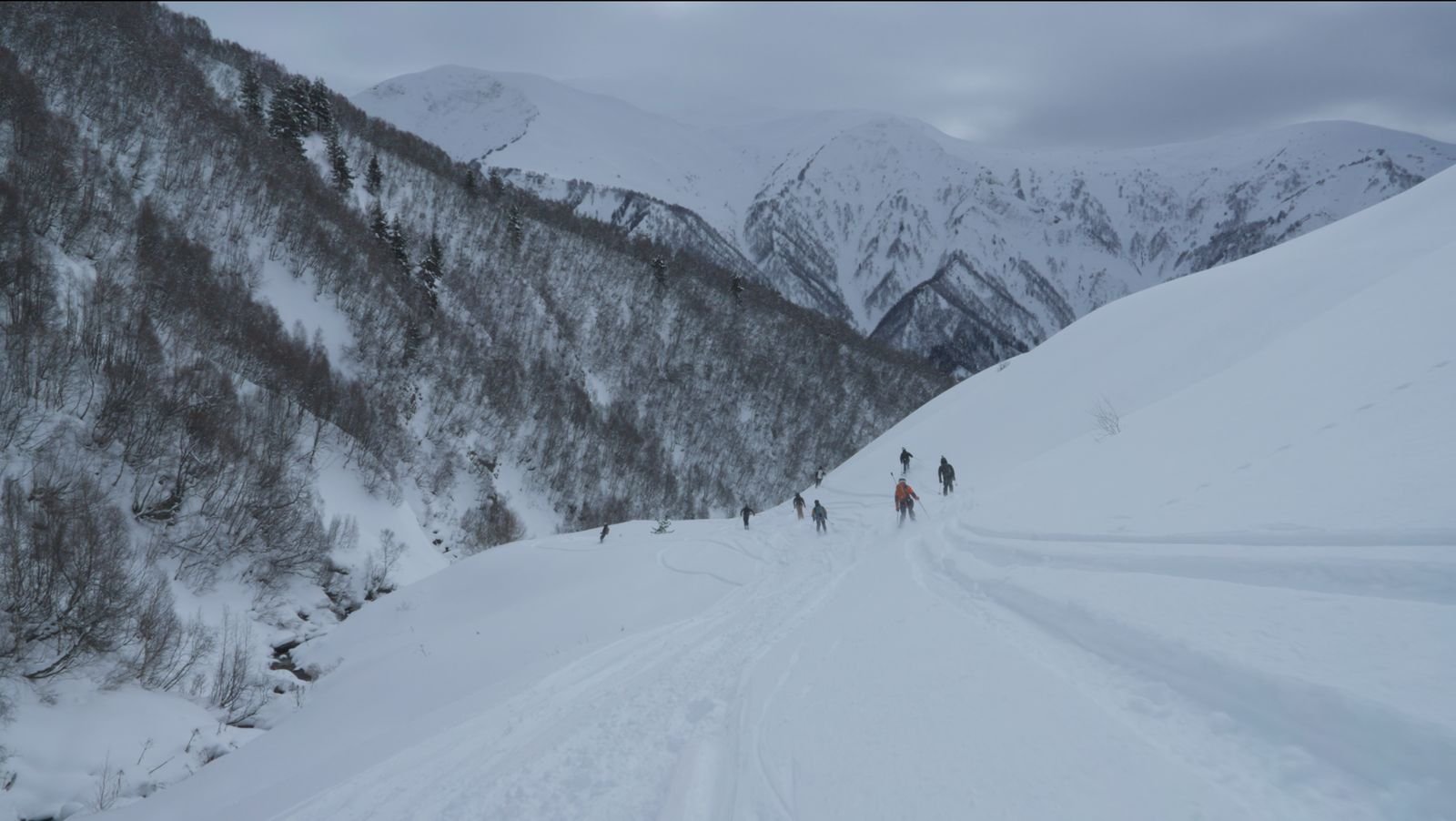 Group of skiers descending a snowy valley between high Caucasus ridges in Svaneti