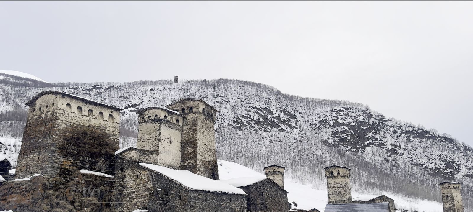 Stone towers of Ushguli under deep snow on an overcast winter day