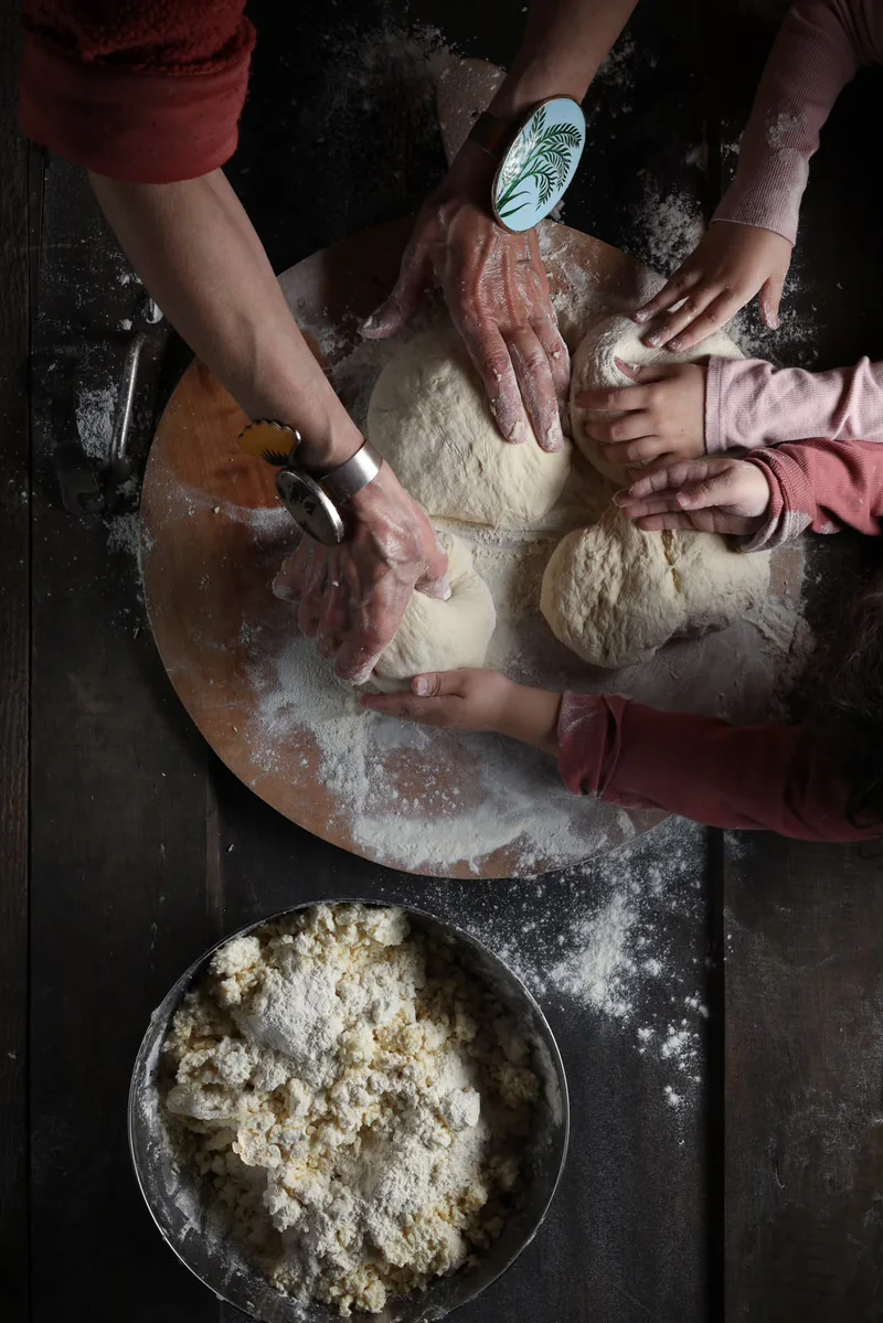 Hands shaping dough together on a flour-dusted wooden board